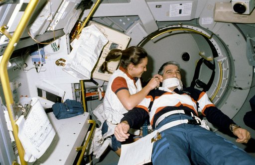 STS-40 MS Jernigan, working at SLS-1 Rack 1, examines Pilot Gutierrez's ear
