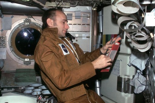 Astronaut Alan Bean reads data from book while holding teleprinter tape