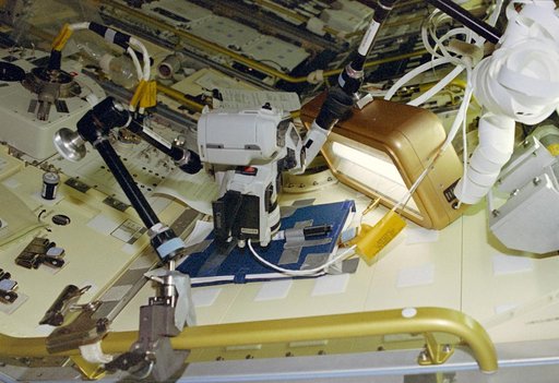 Video camcorder up close to a cylinder attached to a Spacelab locker