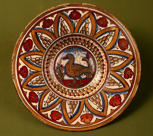 Plate with border of rounded hills within pointed arches with flowers between them; in the center, a wading bird between stylized plants