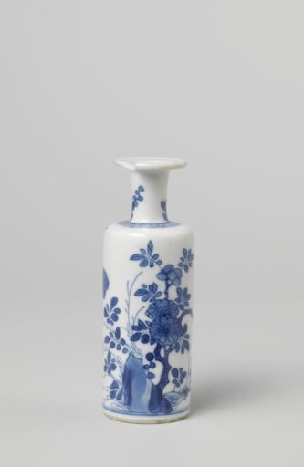 Small cilindrical vase with a flowering plant near a rock