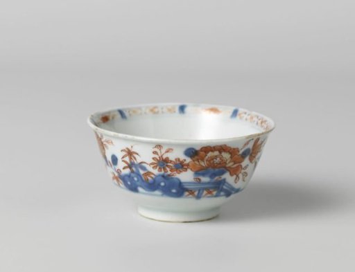 Cup with flower sprays behind a rock and fence