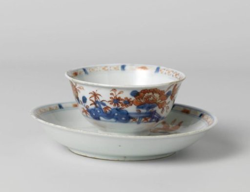 Cup and saucer with flower sprays behind a rock and fence