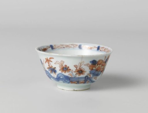 Cup with flower sprays behind a rock and fence
