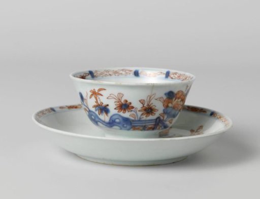 Cup and saucer with flower sprays behind a rock and fence