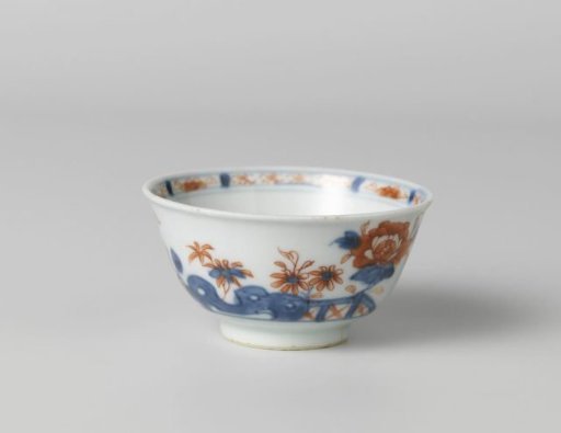 Cup with flower sprays behind a rock and fence