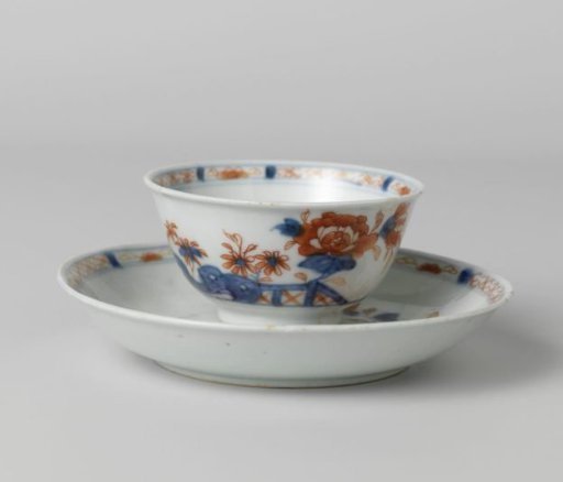 Cup and saucer with flower sprays behind a rock and fence