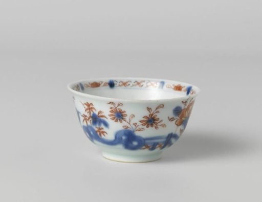 Cup with flower sprays behind a rock and fence