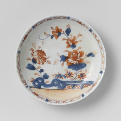 Saucer with flower sprays behind a rock and fence