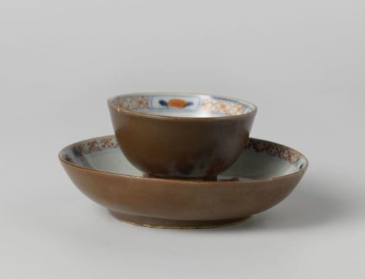 Cup and saucer with flower sprays near a rock and a dark brown glaze