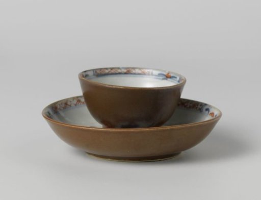 Cup and saucer with flower sprays near a rock and a dark brown glaze