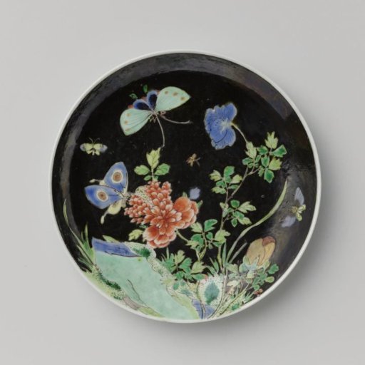 Saucer with butterflies and flowering plant near a rock