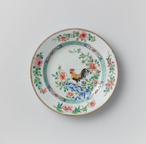 Plate with a cock on a rock near flowering plants
