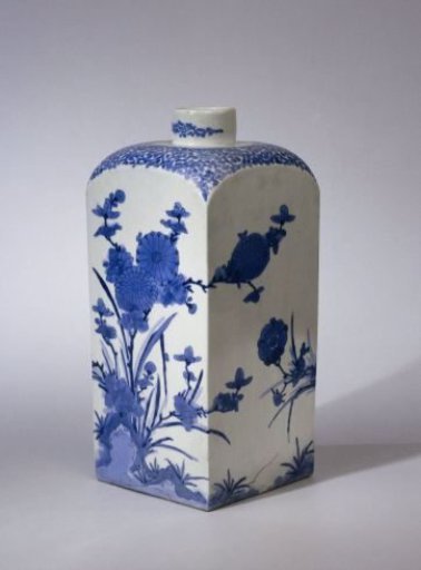 Square bottle with scrolls and flowering plants near rocks