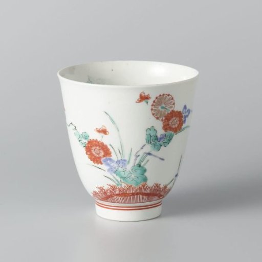 Bell-shaped cup with flowering plants behind a brushwood fence