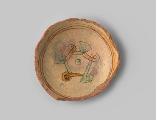 Plate fragment (foot ring) with red-fired body, with yellow glaze on the front and back, with stripes and curls depicted in sgraffito technique in ochre and green glaze