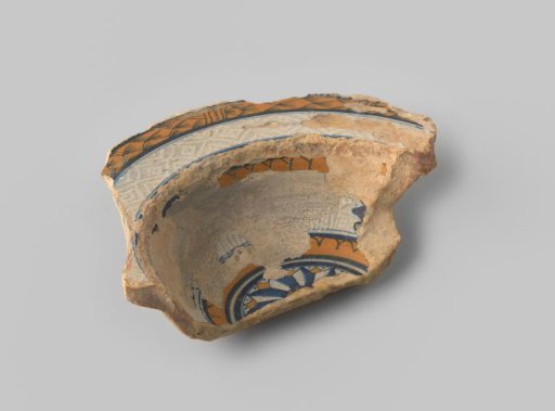 Fragment of a plate with deep base, reddish-yellow sherd, in the central panel a rosette, in blue and orange on a white ground, on the rim geometric figures and a wreath of leaves in white, blue and orange