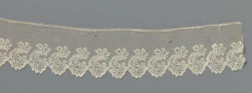 Strip of bobbin lace with a fan-shaped cluster of flowers under a curved leaf