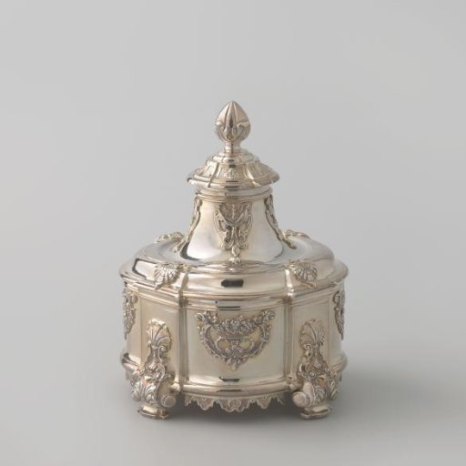 Silver tobacco pot, with rounded corners and projecting pilasters on the sides. Body and lid decorated with Louis XIV appliques. On the lid a leaf finial