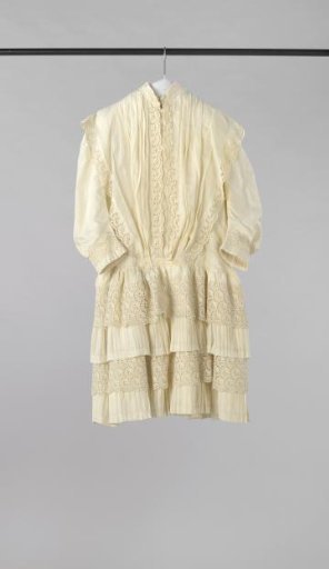Girls' dress with underlayer of white cotton with woven vertical stripes and top layer of white cotton, decorated with pleats, ruches with pleats and borders of English embroidery.