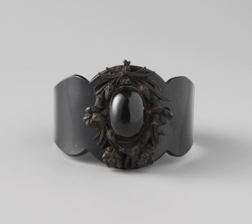 Bracelet of whalebone, broad at the front and somewhat wavy. On the upper side a wreath of flowers and leaves with an oval in the centre.