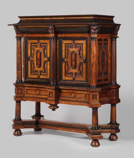 Cabinet with both doors lined with tortoiseshell panels and pilasters in the form of Tuscan columns. Cushion-shaped top with a hinged lid. Carved ornaments as cartouches with strapwork