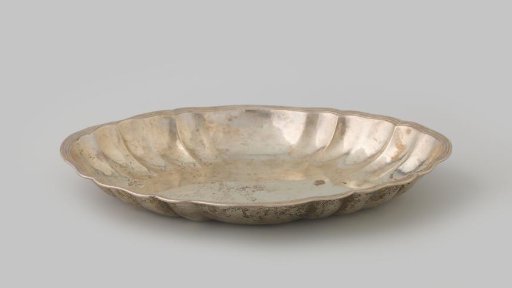 Bread plate of silver. Oval, with chased, fluted lobes and a horizontal scalloped gadrooned rim.