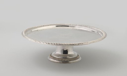 Silver presentation plate, round, edged with a heavy cable border. On the field a lozenge-shaped coat of arms between two crossed plumes. Short, round foot.