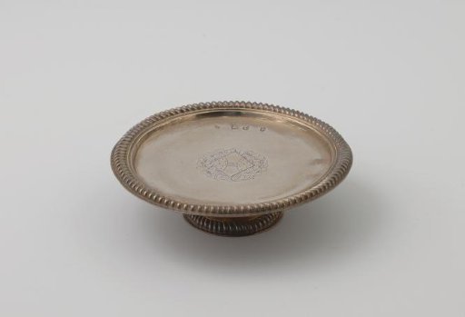 Silver presentation plate, round, edged with a heavy cable border. On the field a lozenge-shaped coat of arms between leaf and cartouche motifs. Short, round foot.