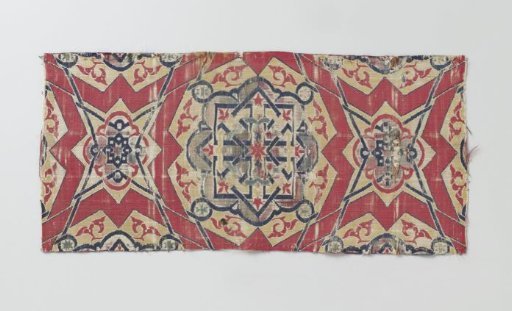 Fragment of red lampas with a multicolored pattern of geometric figures and blue braiding