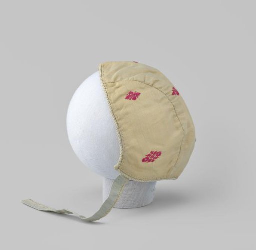 Children's cap of pale yellow changeant silk with a red flower