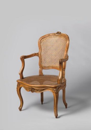 Armchair of walnut with S-shaped legs placed diagonally and with a back and seat of cane. Carving of flowers and leaves. With a loose cushion. Set of eight pieces.