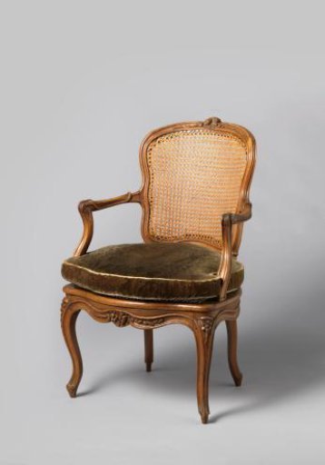 Armchair of walnut with S-shaped legs placed diagonally and with carving of flowers and leaves. Back and seat of woven cane. With a loose cushion.