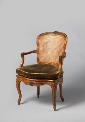 Armchair of walnut with S-shaped splayed legs with carving of flowers and leaves. Back and seat of woven reed. With loose cushion.