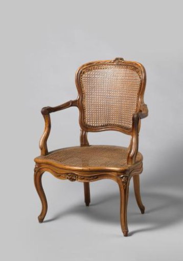 Armchair of walnut with S-shaped splayed legs with carving of flowers and leaves. Back and seat of woven reed. With loose cushion.