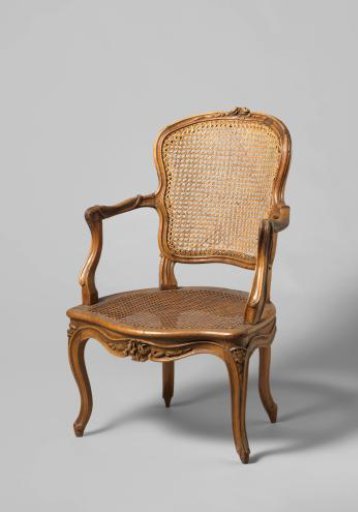 Armchair of walnut with S-shaped splayed legs with carving of flowers and leaves. Back and seat of woven reed. With loose cushion.