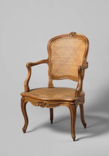 Armchair of walnut with S-shaped splayed legs with carving of flowers and leaves. Back and seat of woven reed. With loose cushion.