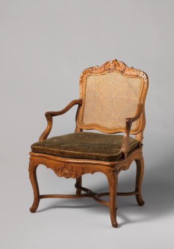 Armchair of walnut and beech wood with S-shaped splayed legs; X-shaped cross with rosette; carved floral and foliate motifs, wicker back and seat, with loose cushion