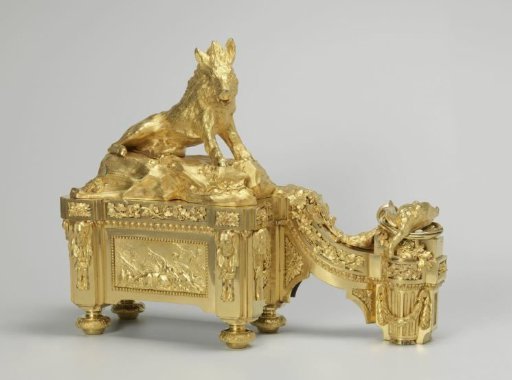 Fire dog of gilded bronze with animal heads, rosettes, grapevines, and a hunting scene featuring a stag and shot game on a rectangular base