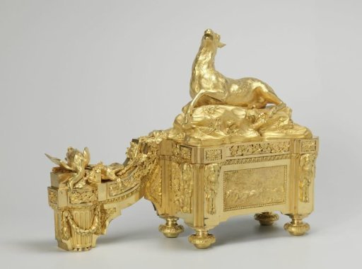Fire dog of gilded bronze with dog heads, rosettes, grapevines, and a hunting scene on a rectangular base; a boar and shot game with a hunting horn.