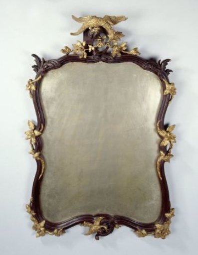 Mirror in a profiled and carved frame with floral swags, rocaille motifs and a bird (pelican?) in the center. Brown painted and partially gilded wood.