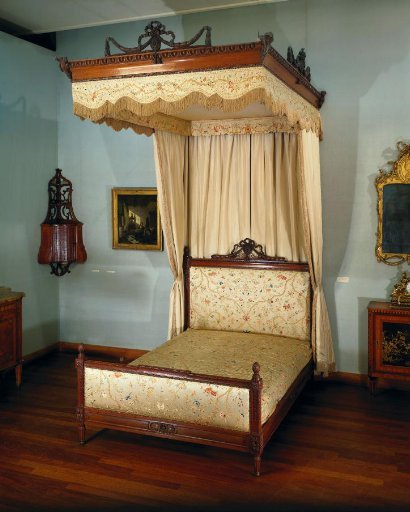 Bracket-shaped scalloped strip of cream-white satin, embroidered in color with a rosette and a winding vine
