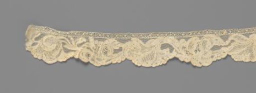 Cuff of needle lace with a symmetrical pattern with a flower vase, vines with feathered leaves and irises
