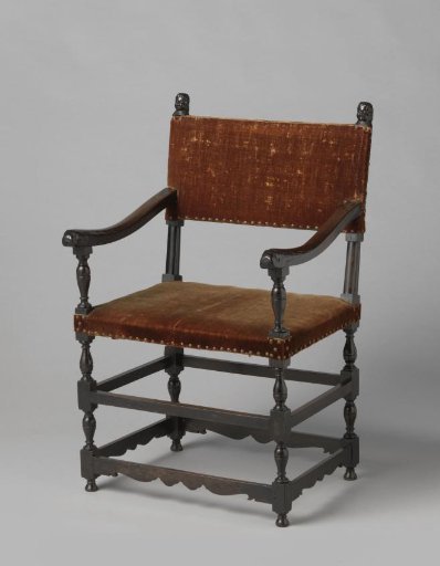 Armchair of ebony with hollowed armrests ending in stylized dolphin heads on vase-shaped armrest supports. Back splats with cherubs.