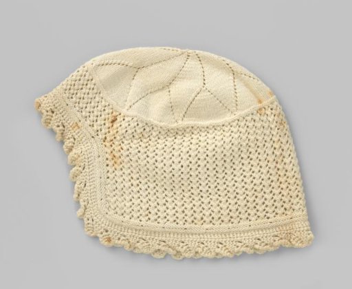 Knitted white cotton children's cap (?), with openwork, scalloped edge and on top a large floral motif with an opening in the middle