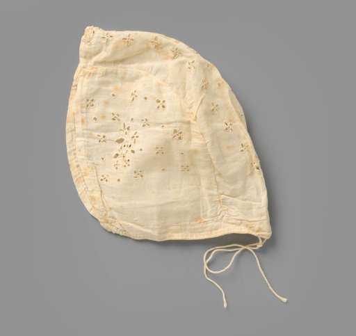 White cotton children's cap with open embroidery with floral motifs; at the back two cords