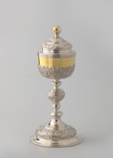 Ciborium of silver with gilded cup and finial. Arched foot and cover; baluster stem. Decoration along the edges with symmetrical rocailles on punched ground.