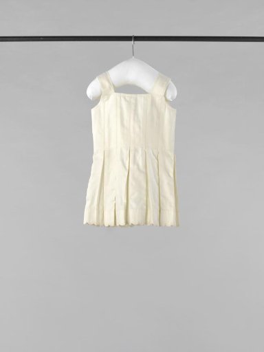 Sleeveless children's dress or monkey coat of white twill cotton with bodice of densely stitched flat pleats and back closure with three bows, scalloped hem