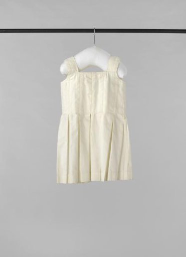 Children's dress of sturdy white cotton twill, with back split and three ribbon ties, wide shoulder straps and pleated skirt