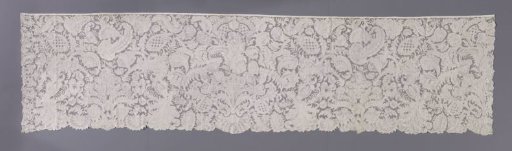 Strip of an alb of needle lace with pomegranates and feathers and centrally a scallop shell